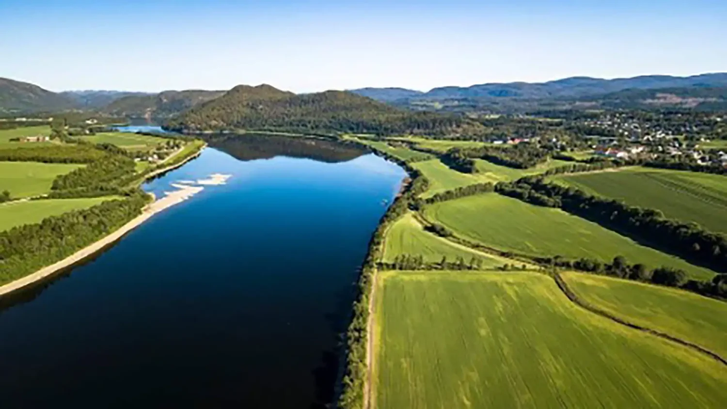 Namsen med Hunn (høgre) og Førrinesset (venstre) og Vattan i bakgrunn. Ned til høgre ligger bekken der det tidligere var et elveløp slik kartet til Sommerschield viser. Skogteigen til venstre er den tidligere øya utenfor Førri og som fikk landkontakt ved raset i 1959 med smalere elveløp som resultat. Foto: Einar Aas